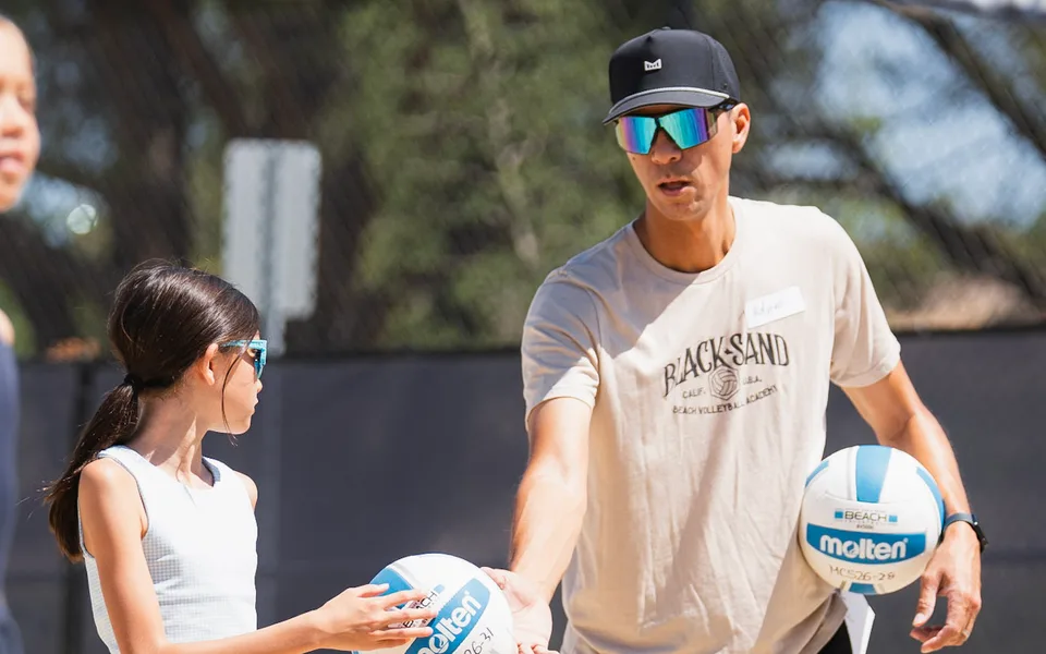 Coach Adam Black hands a ball to a young player at a Black Sand clinic
