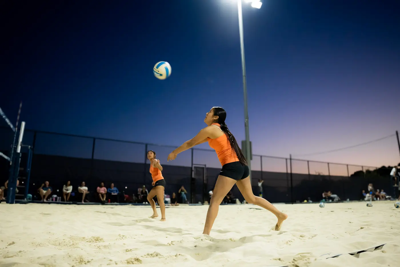 A player serves as the court lights come on