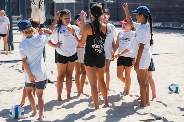 Campers in white camp shirts huddle on the sand