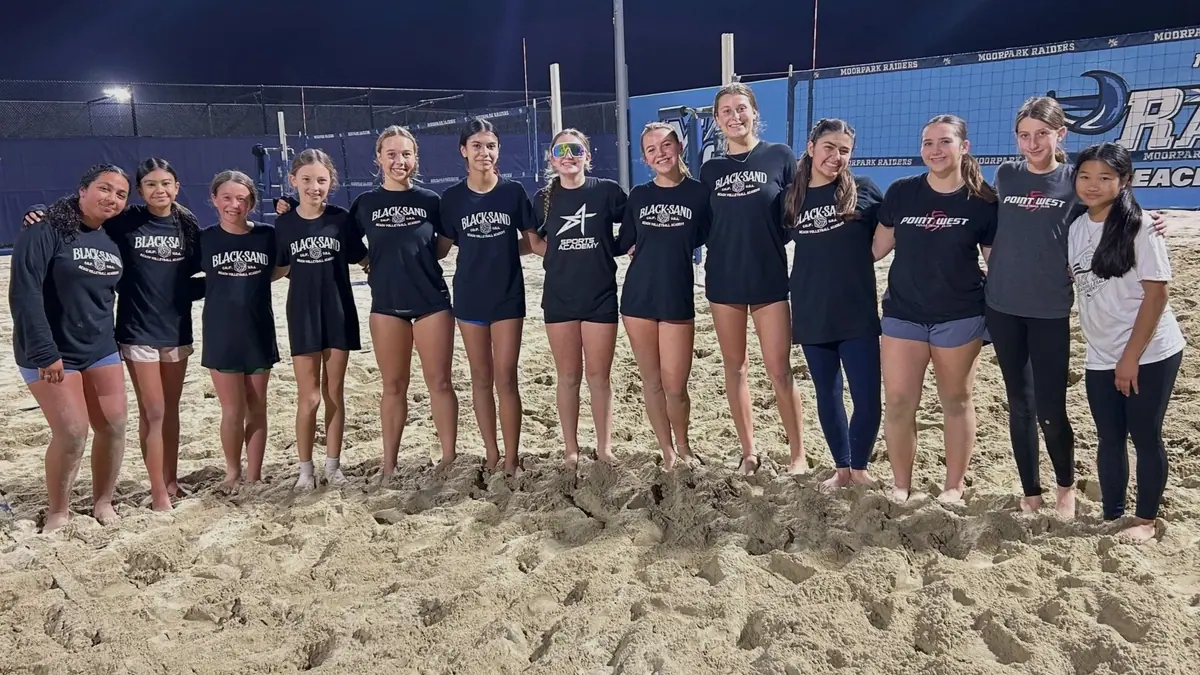 Players line up for a team photo on the floodlit sand courts at night