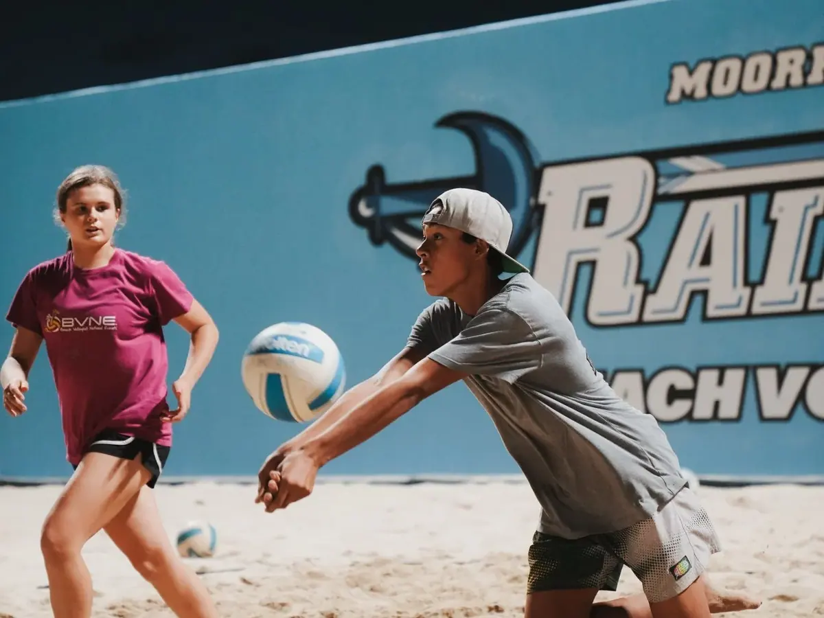 Two players dig balls on the sand in front of the Moorpark Raiders windscreen