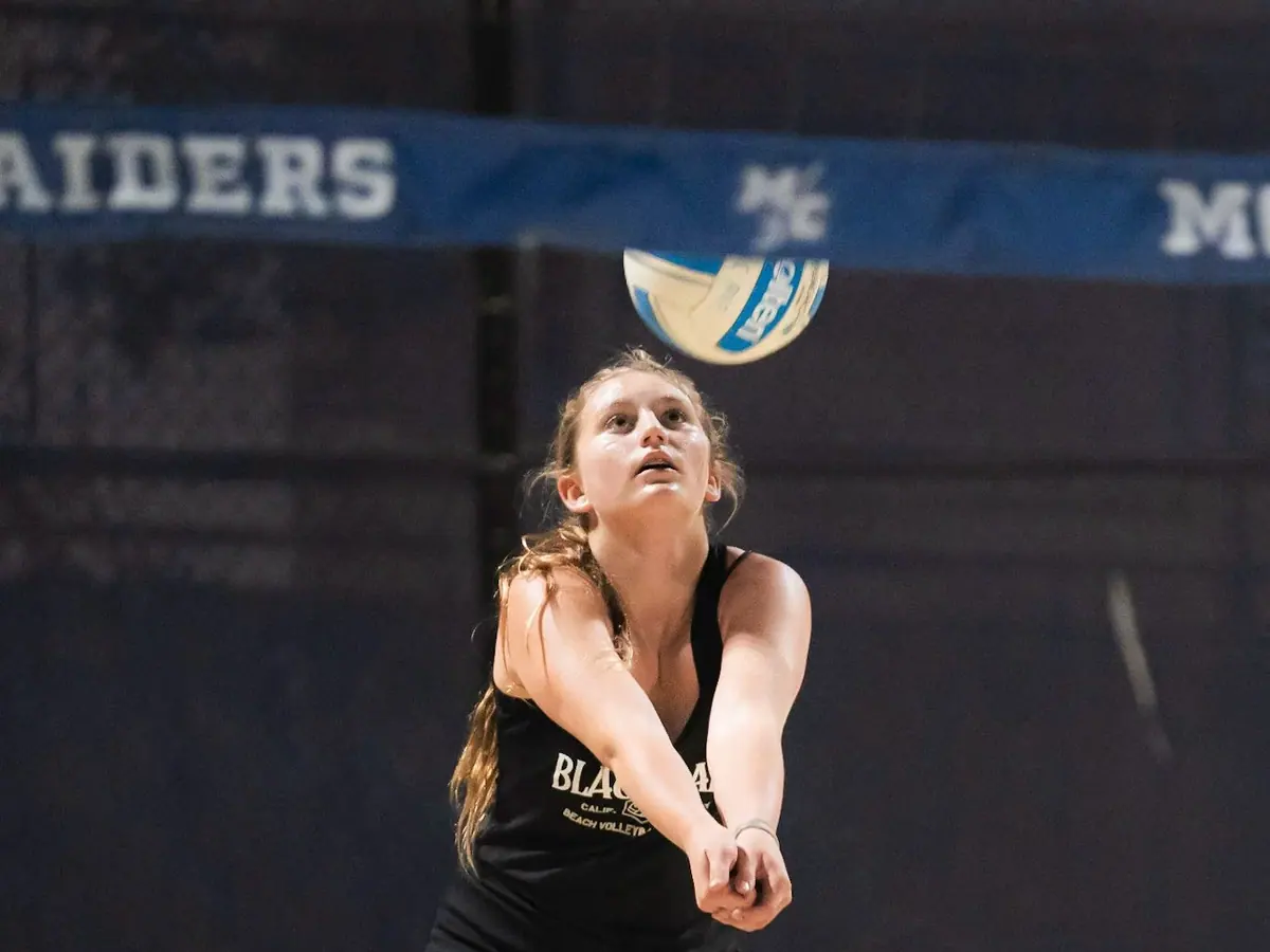 A player in a Black Sand top passes a ball on the sand court