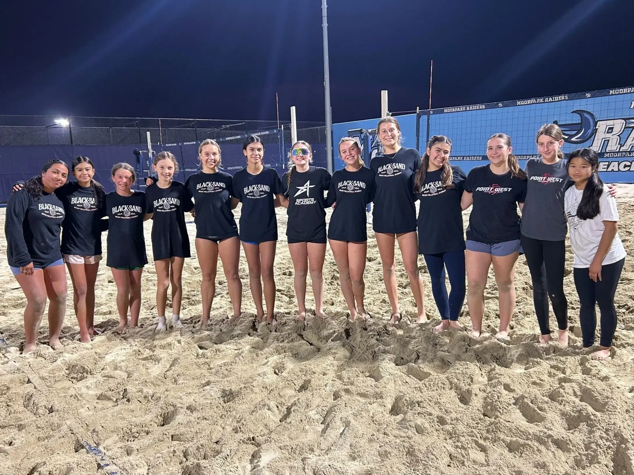 Players line up for a team photo on the floodlit sand courts at night